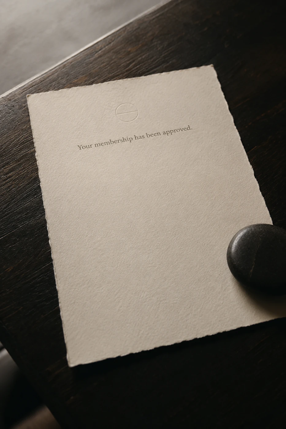 A Solis welcome letter on deckle-edged cotton paper: an embossed mark and the line your membership has been approved, a dark stone weight at one corner